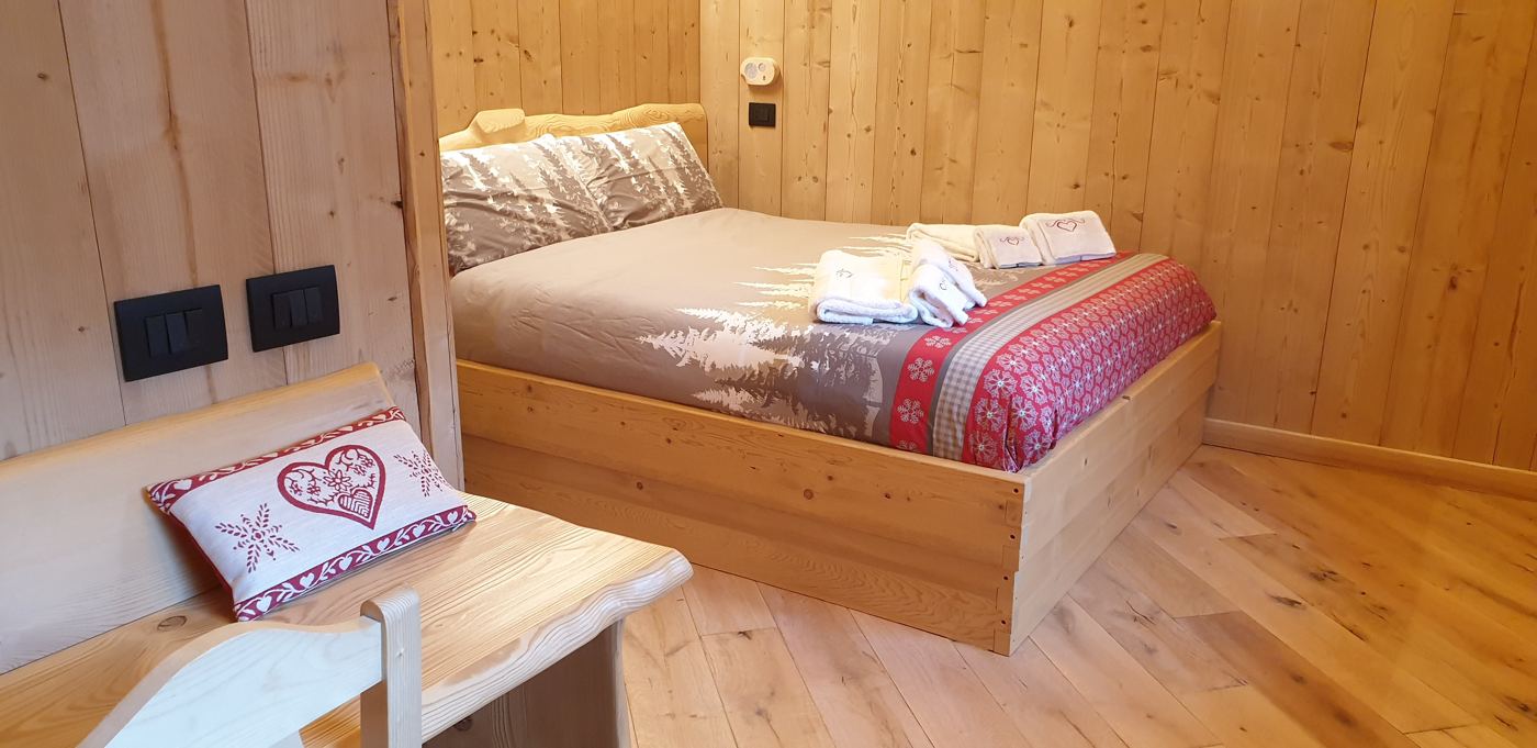 Camera matrimoniale con rivestimenti in legno e biancheria con abeti e fantasie rosse