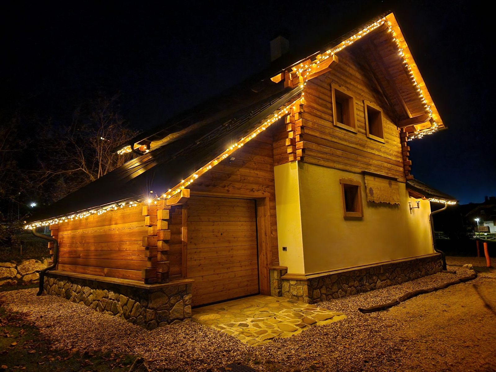 La baita di legno e intonaco di notte, con le luci accese lungo il tetto e il basamento in pietra
