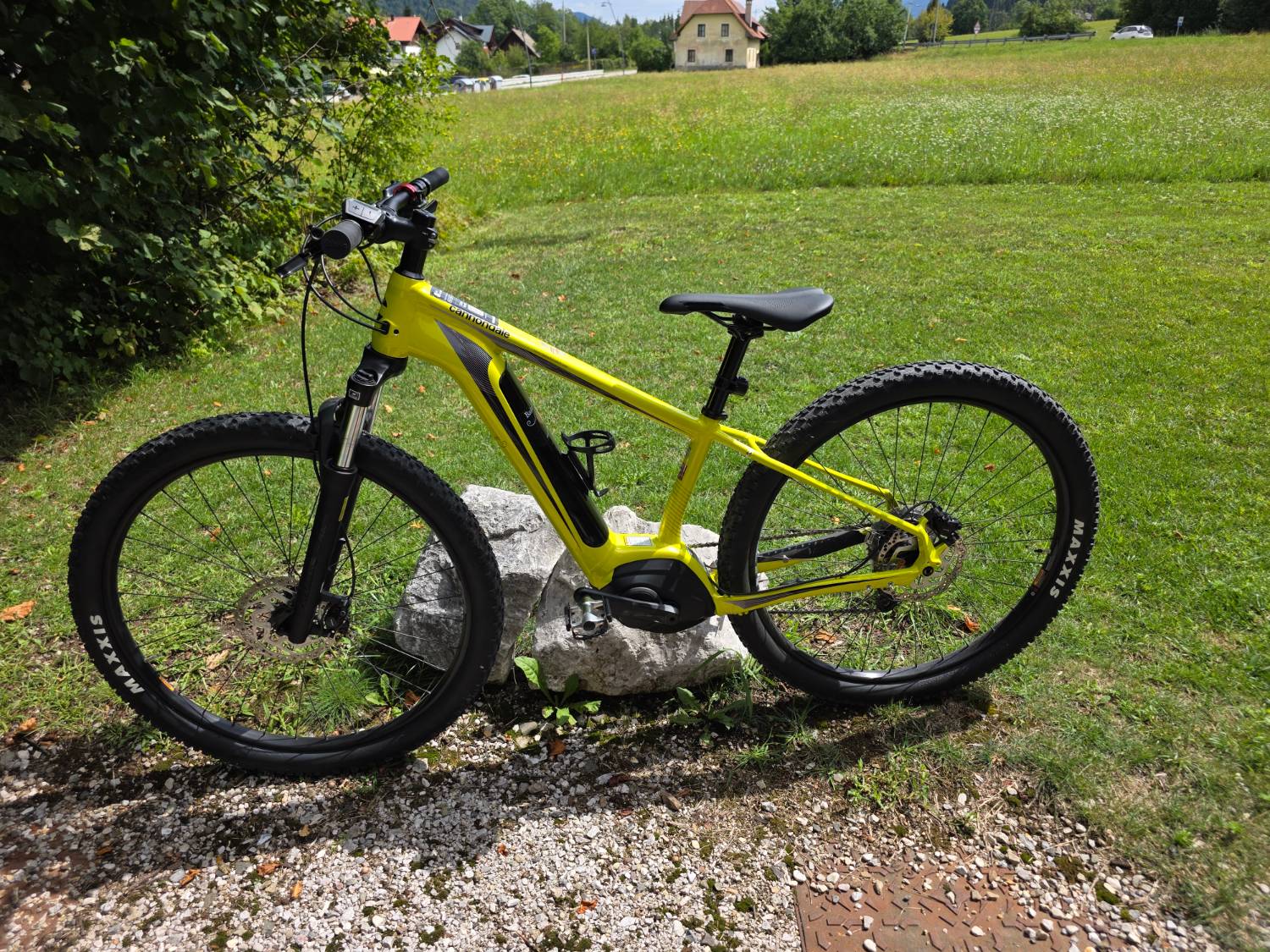Una e-bike gialla appoggiata a una roccia in un prato verde, con le montagne sullo sfondo