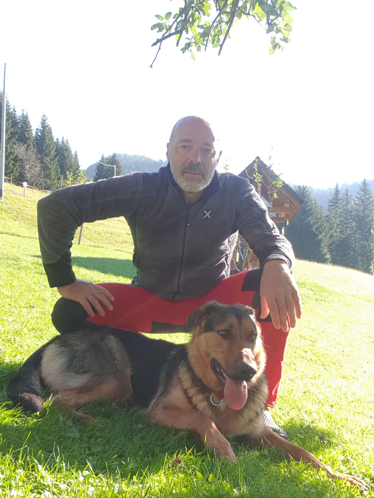 Daniele Traunero, guida ambientale escursionistica, seduto su un prato di montagna accanto al suo cane