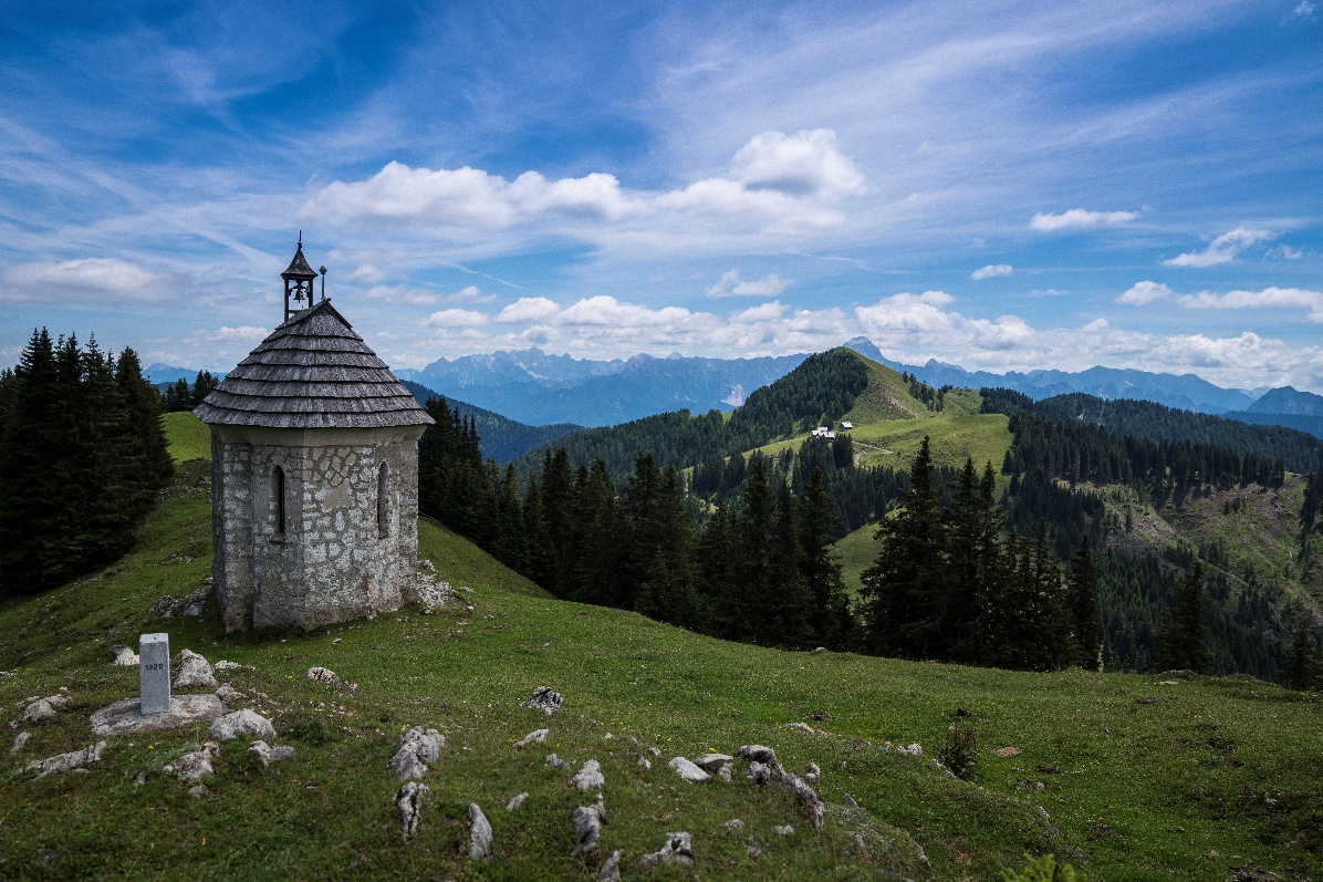 La cappella della Madonna della Neve in cima a un prato, con le Alpi Giulie sullo sfondo
